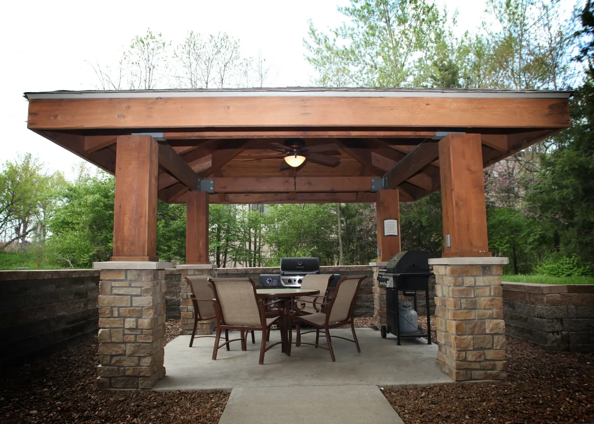 This exterior shot captures a wooden gazebo with a dining table and grill, creating an inviting setting for outdoor meals and social gatherings. The relaxed mood and evening lighting hint at sunset dinners and memorable celebrations.