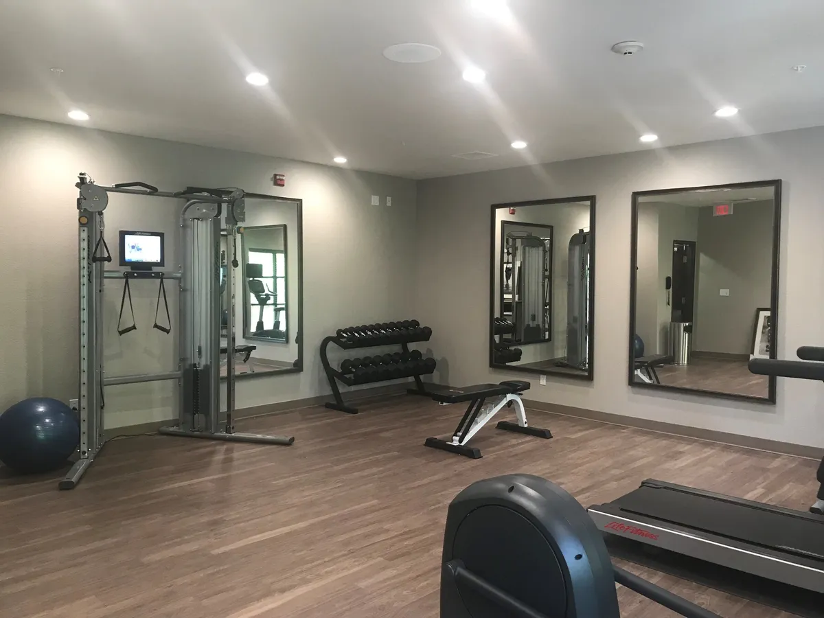 This image showcases an energetic, well-equipped fitness center featuring weight lifting equipment, a treadmill, an exercise ball, and large mirrors that create a sense of spaciousness. The scene captures an environment conducive to working out, personal training, or group fitness classes, conveying a vibrant and active atmosphere.