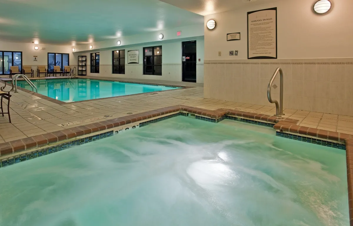 An indoor pool area with a tranquil hot tub, ambient lighting, and a comfortable seating area. The rejuvenating environment suggests a space for unwinding and self-care, reinforcing the spa-like ambiance described in the section.